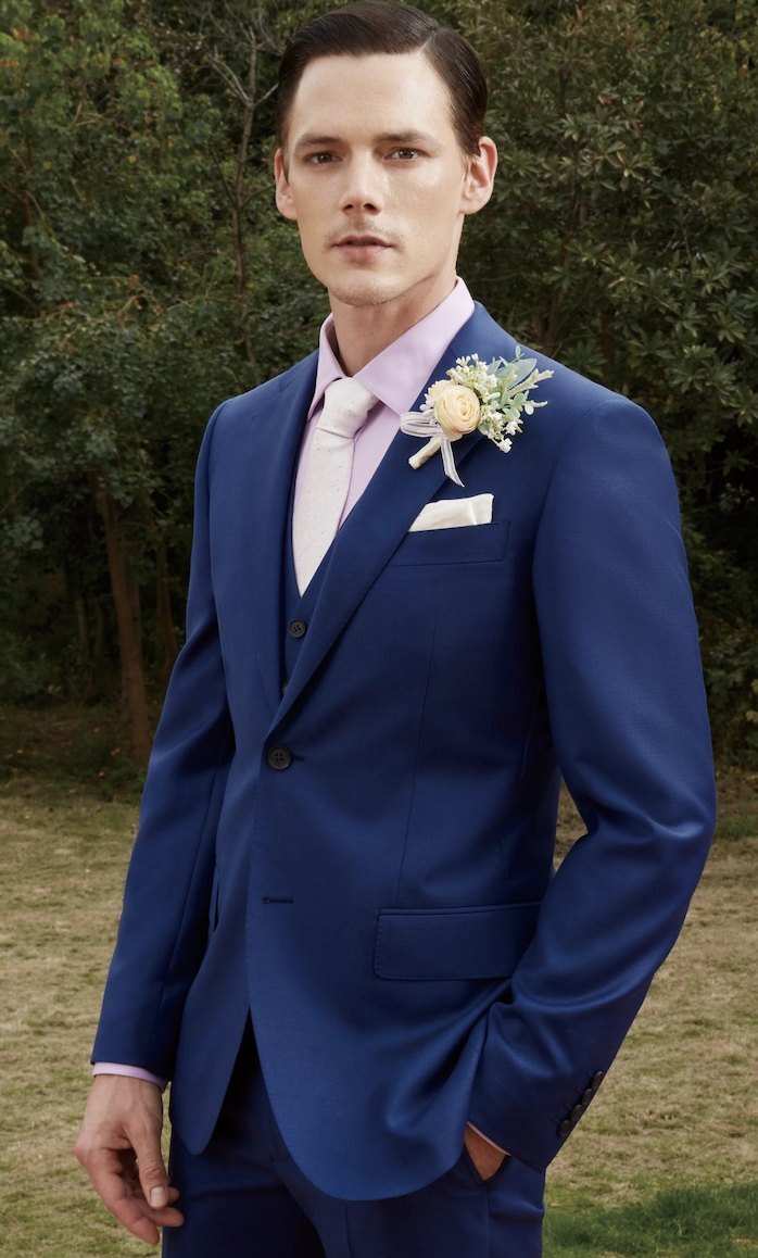 Costume bleu roi, cravate rose pâle et fleur à la boutonnière, dans un jardin