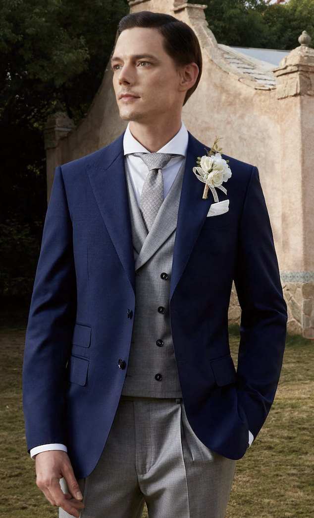 Jaquette bleu marine, gilet gris perle, cravate argent et fleur à la boutonnière, dans un jardin