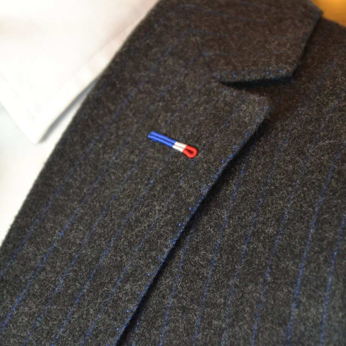 Revers d'une flanelle anthracite à fine rayure bleue : boutonnière milanaise bleu, blanc, rouge et surpiqûres le long du revers