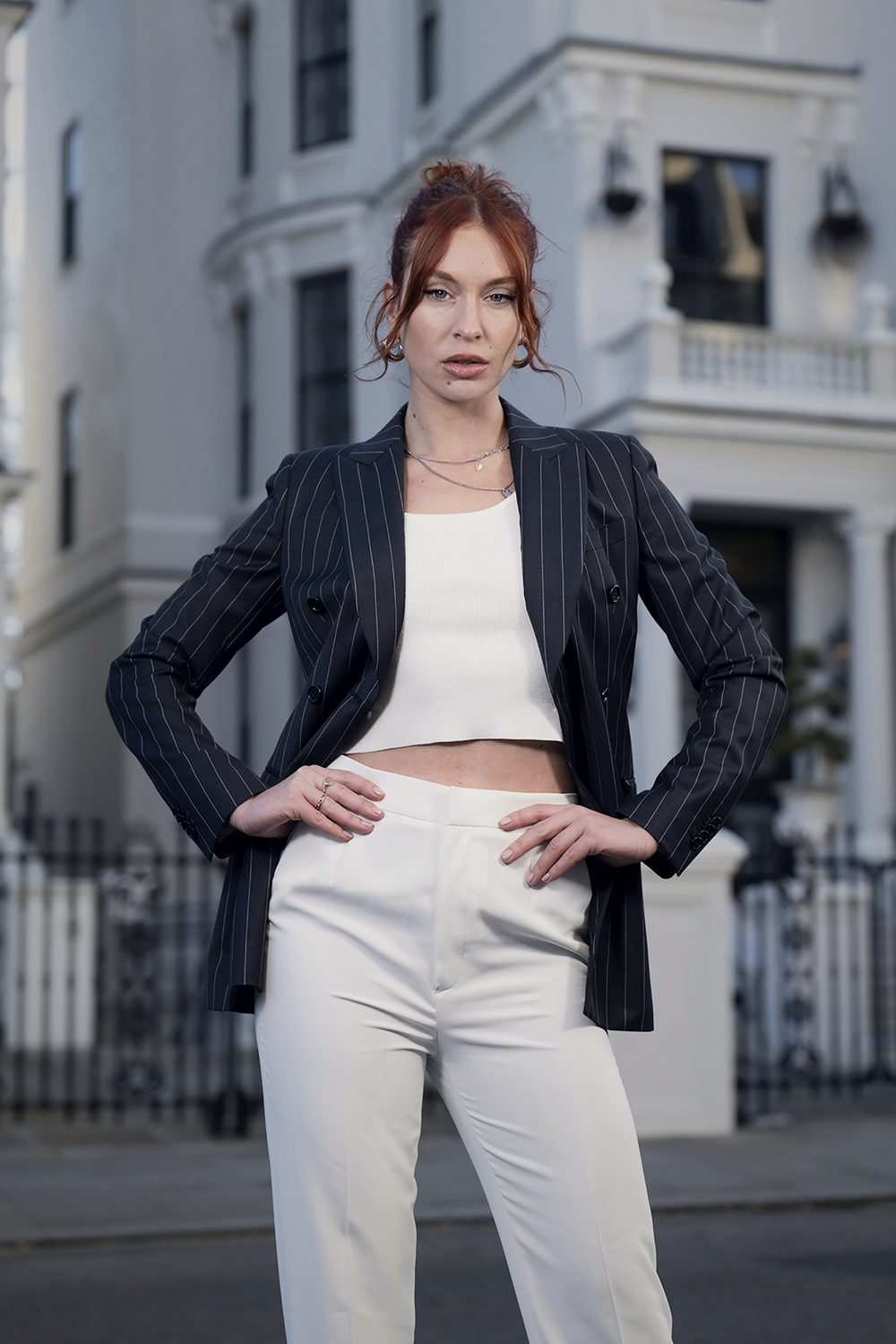 Femme en veste croisée anthracite à rayures tennis et pantalon blanc, dans la rue