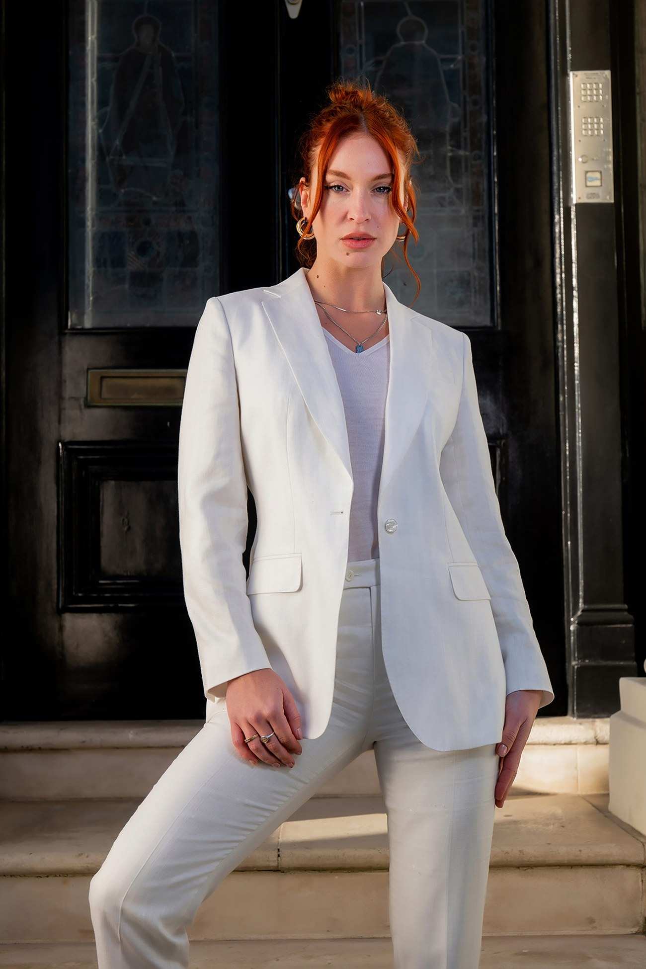 Tailleur pantalon blanc porté sur un top blanc, devant une porte noire