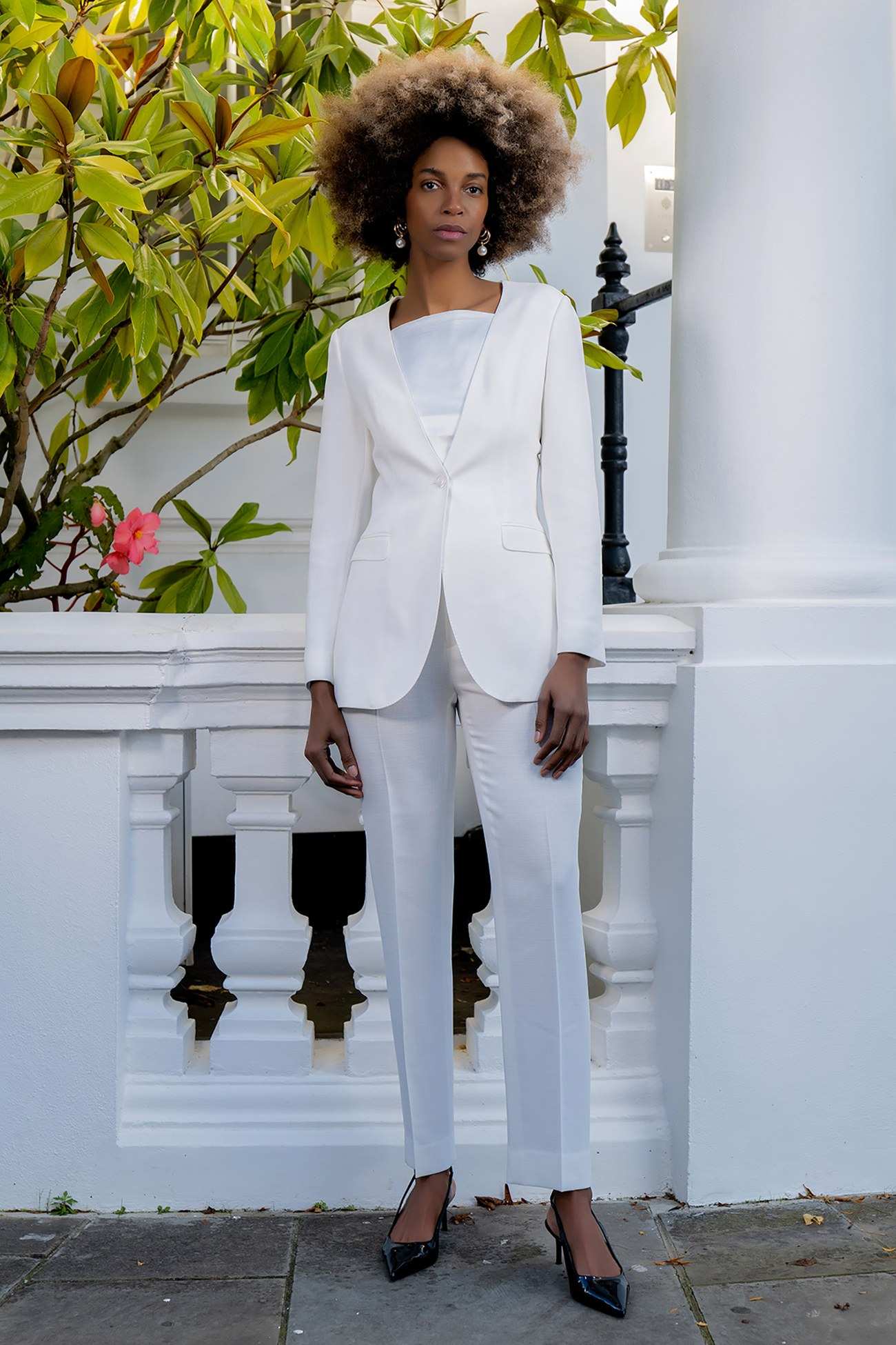 Tailleur pantalon blanc et escarpins noirs, sur une terrasse blanche fleurie