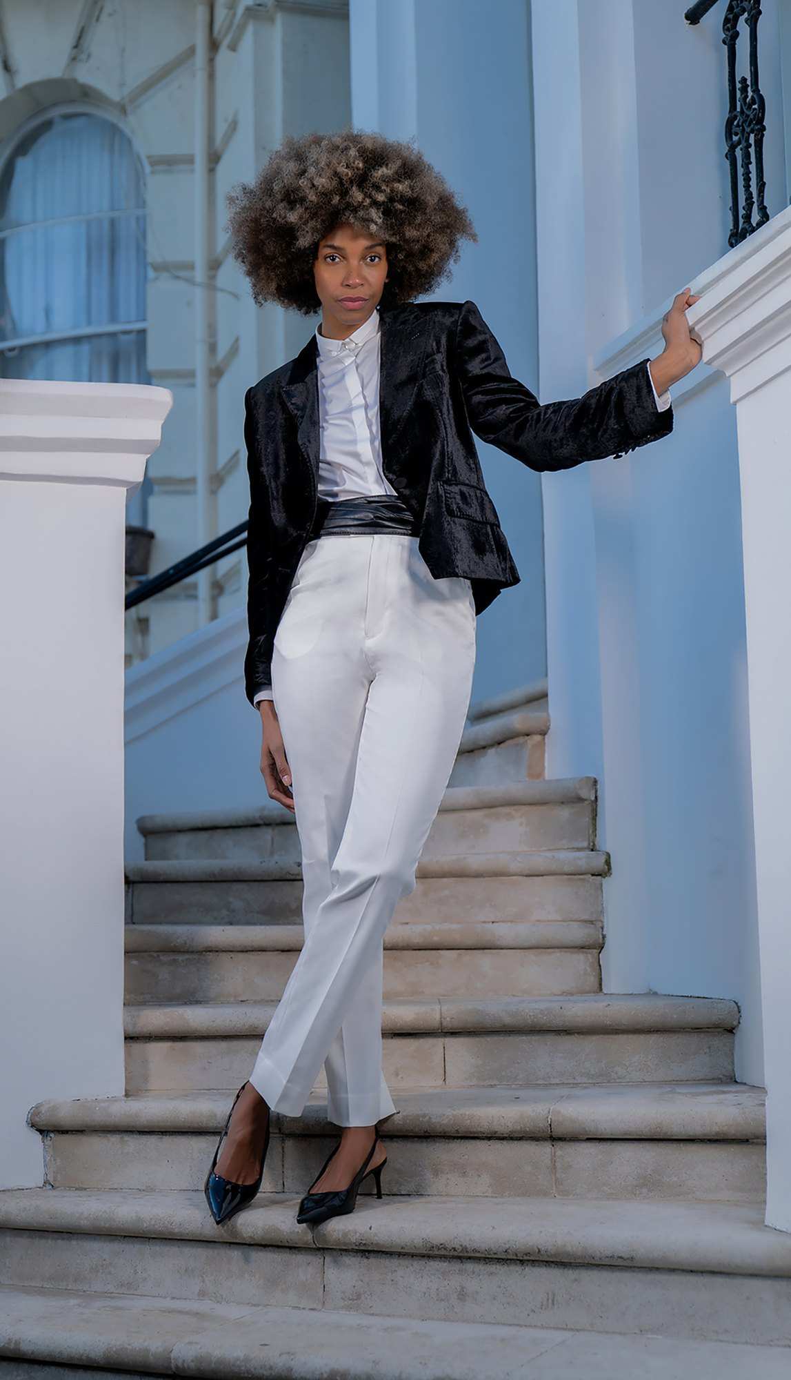 Veste de satin noir et pantalon blanc, dans un escalier de pierre blanche
