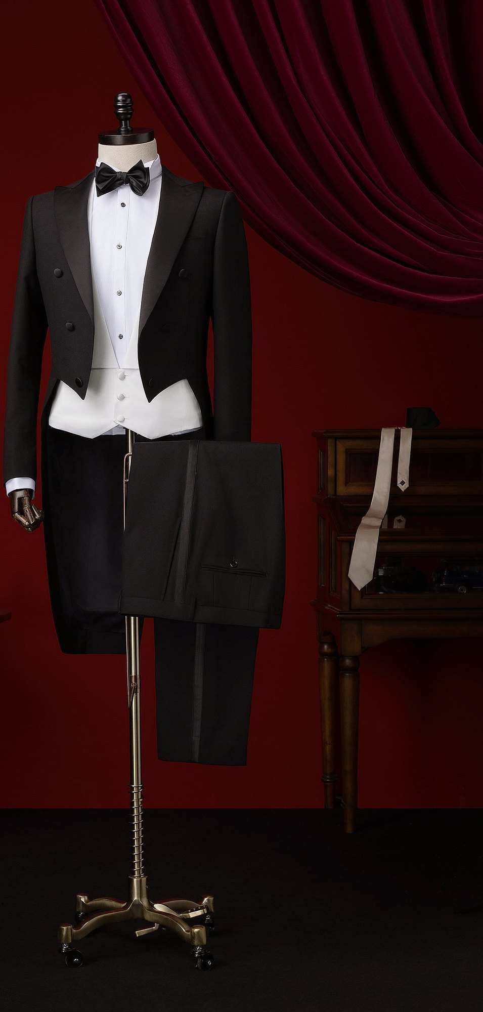 Habit noir à queue-de-pie, gilet blanc, nœud papillon et pantalon à galon, sur un buste devant un rideau rouge