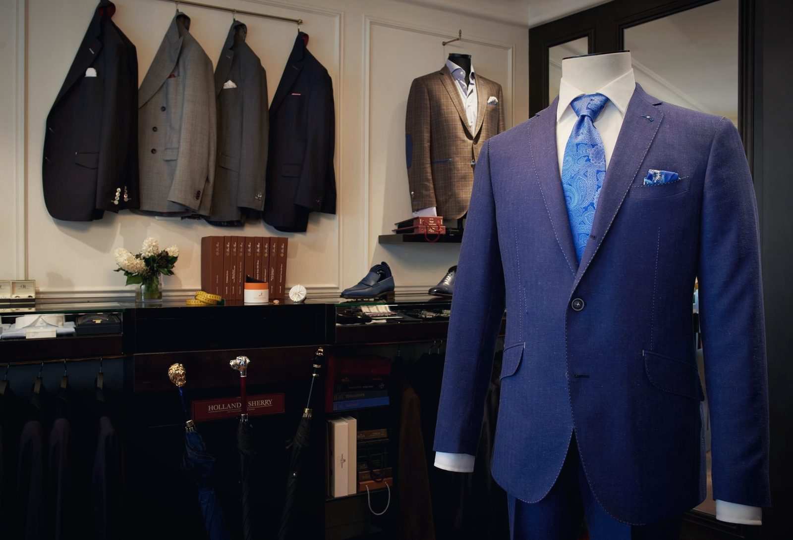Costume bleu sur buste dans la boutique, vestes accrochées et accessoires en vitrine